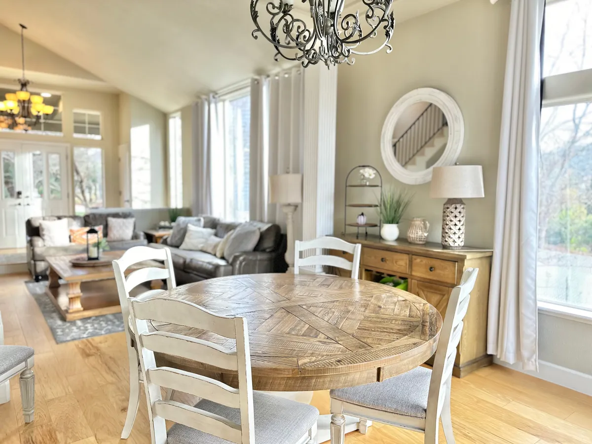 The room features a cozy round wooden dining table under an elegant chandelier, with comfortable seating and large windows providing ample natural light. The adjacent sofa area offers space for informal gatherings or peaceful solo moments—perfect for balancing productivity and relaxation.