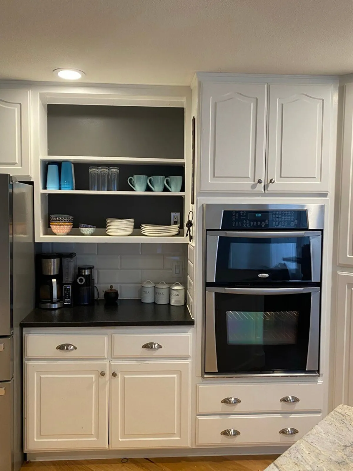 A welcoming kitchen with white cabinetry, sleek black countertops, modern kitchen appliances, and open shelving with dishware. The layout suggests a space tailor-made for group meal prep, casual brunches, and social cooking. The coffee maker and ample counter space highlight the kitchen's functionality for hosting and shared meals.