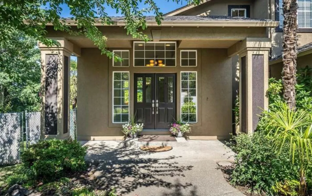 The image shows a welcoming view of the home's double front doors, framed by well-arranged windows and potted plants. The entryway is inviting and framed by greenery, hinting at a family-friendly environment and the home's connection to the outdoors.