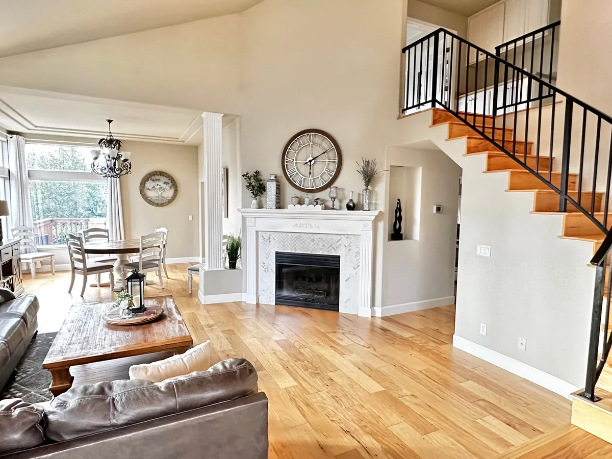 A cozy, open-plan living and dining area with a central fireplace, a large dining table for festive meals, a staircase, and inviting décor. The space is set up for group socializing, with plenty of seating and a warm, comfortable vibe—ideal for relaxing evenings or lively gatherings.