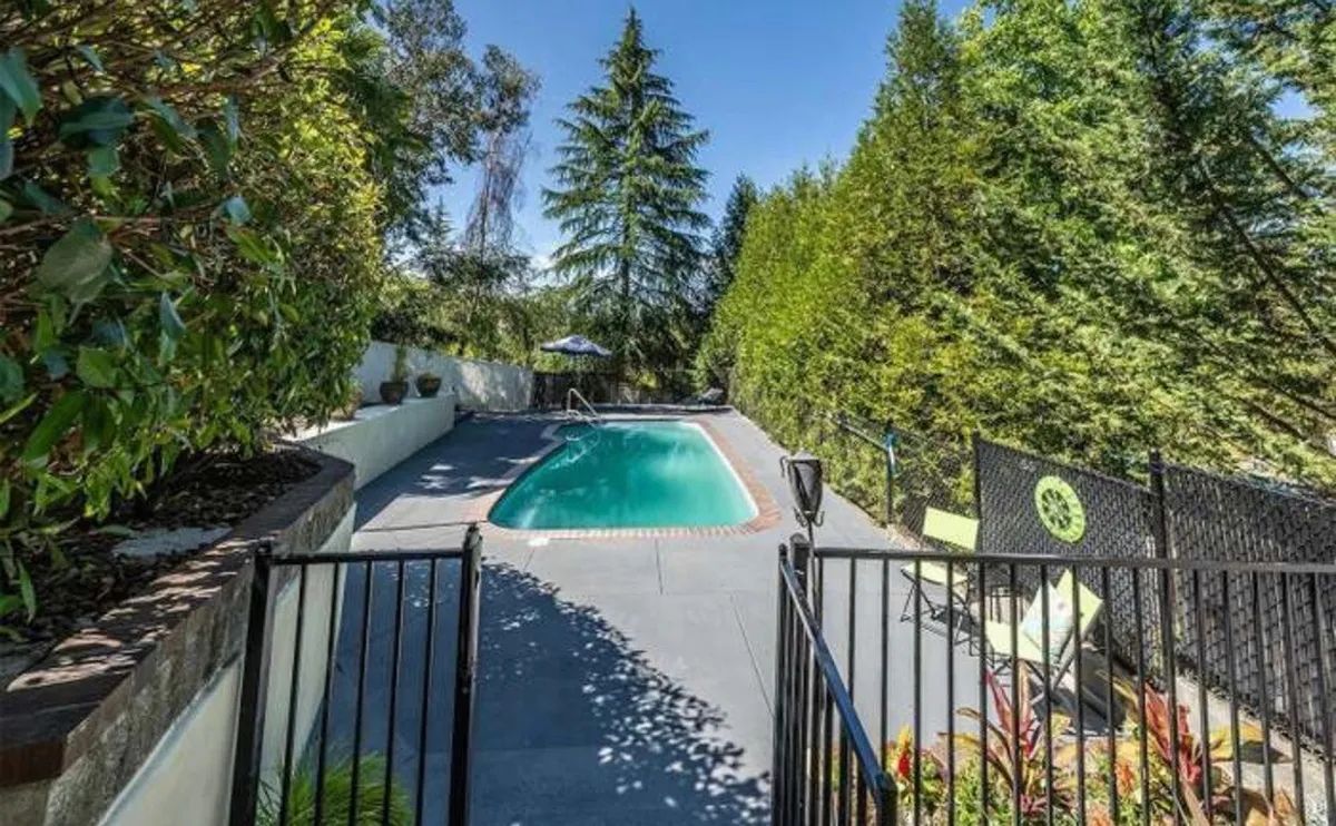 This image captures a serene outdoor swimming pool surrounded by lush greenery, with a secure fence and comfortable lounge chairs. The setting highlights the possibility of family fun—swimming, sunbathing, and relaxing after a day exploring Medford.