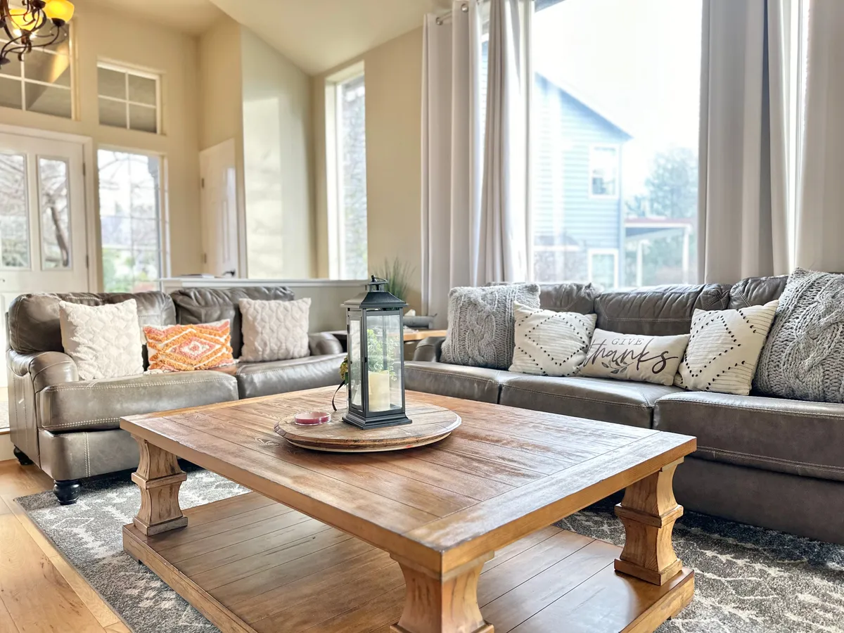 A cozy family room with plush sofas, a coffee table, decorative lantern, and windows letting in abundant natural light. The arrangement invites conversation and relaxation, embodying a warm atmosphere.