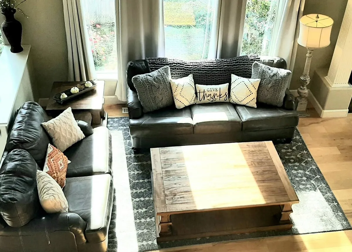 A welcoming living space featuring leather sofas, a wooden coffee table, and decorative pillows, all set around large windows that flood the room with light. The ambiance is both stylish and homey.