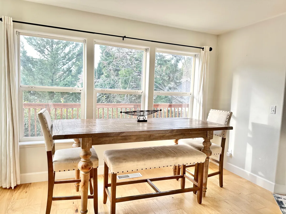 A bright dining area featuring a wooden table, modern bar stools, and expansive windows that let in ample sunlight. The atmosphere is cozy and welcoming, ideal for group breakfasts or evening dinners.
